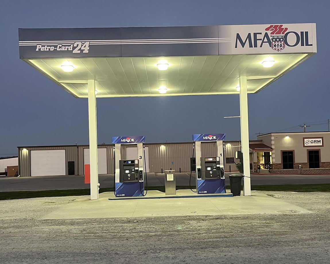 A Petro-Card 24, well-lit MFA Oil gas station with two fuel pumps under a canopy at dusk. The sign reads Petro-Card 24. Industrial buildings are visible in the background.